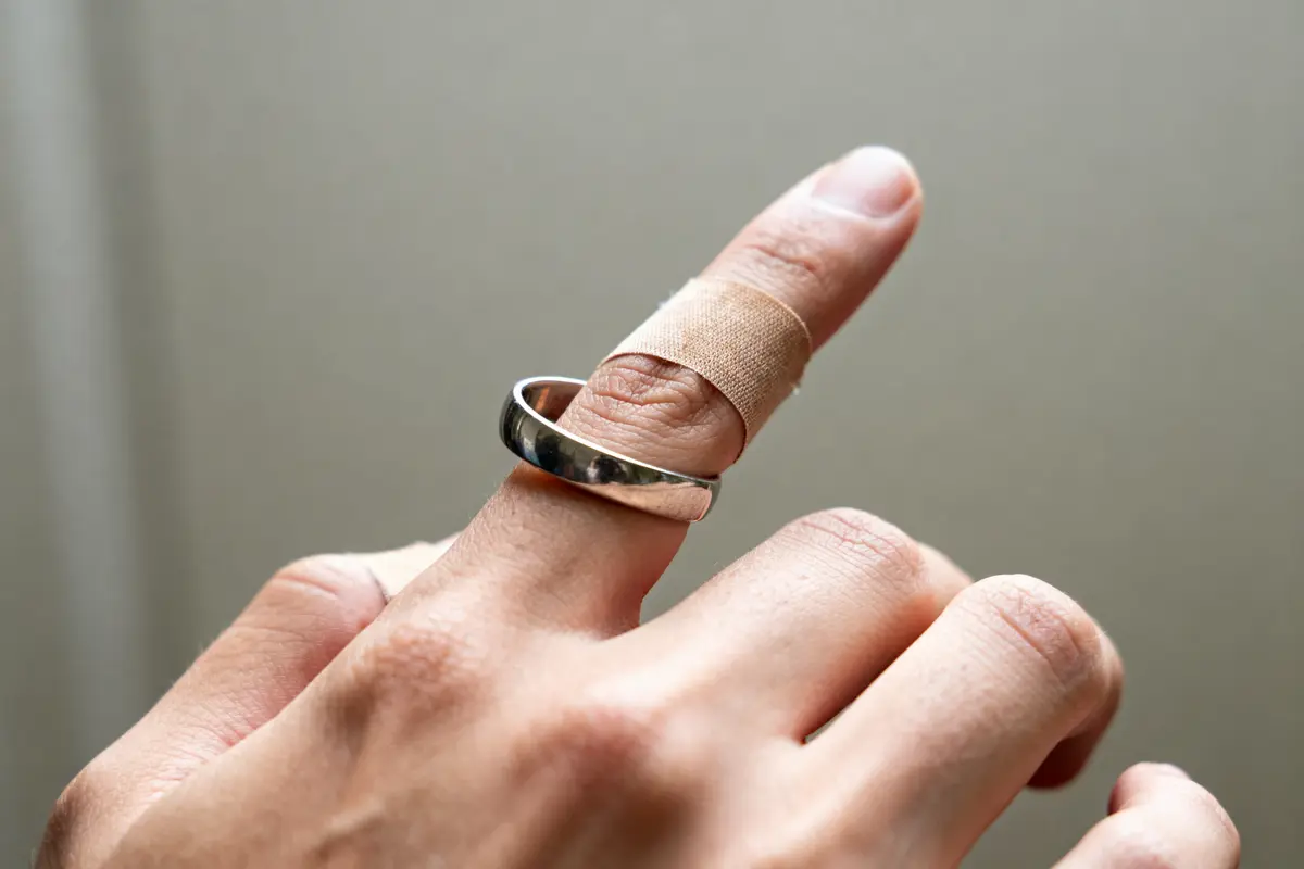 Doigt bandé portant une bague qui tourne en métal argenté sur fond neutre